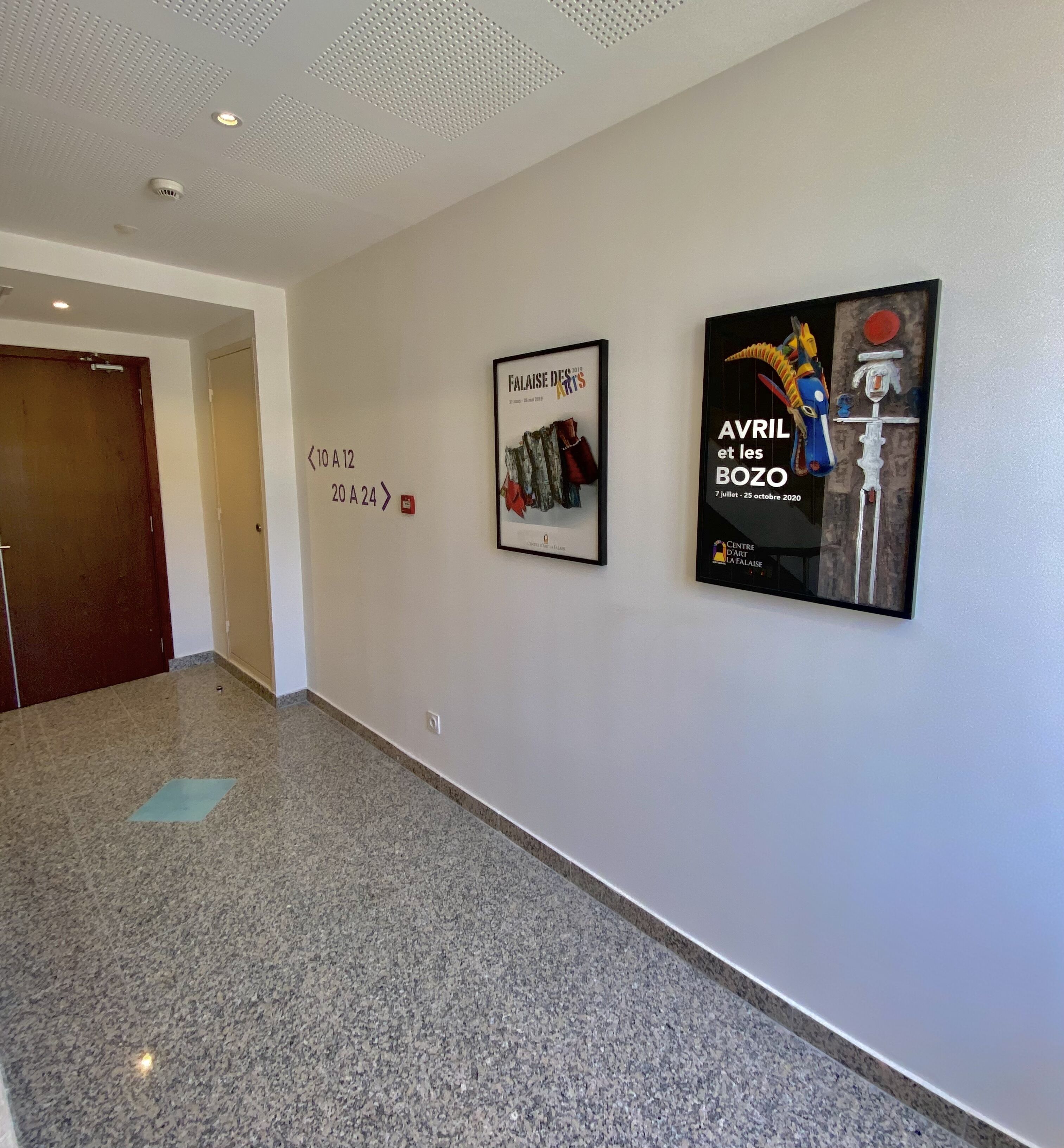 Un pasillo con dos carteles en la pared, un detector de incendios y una puerta.