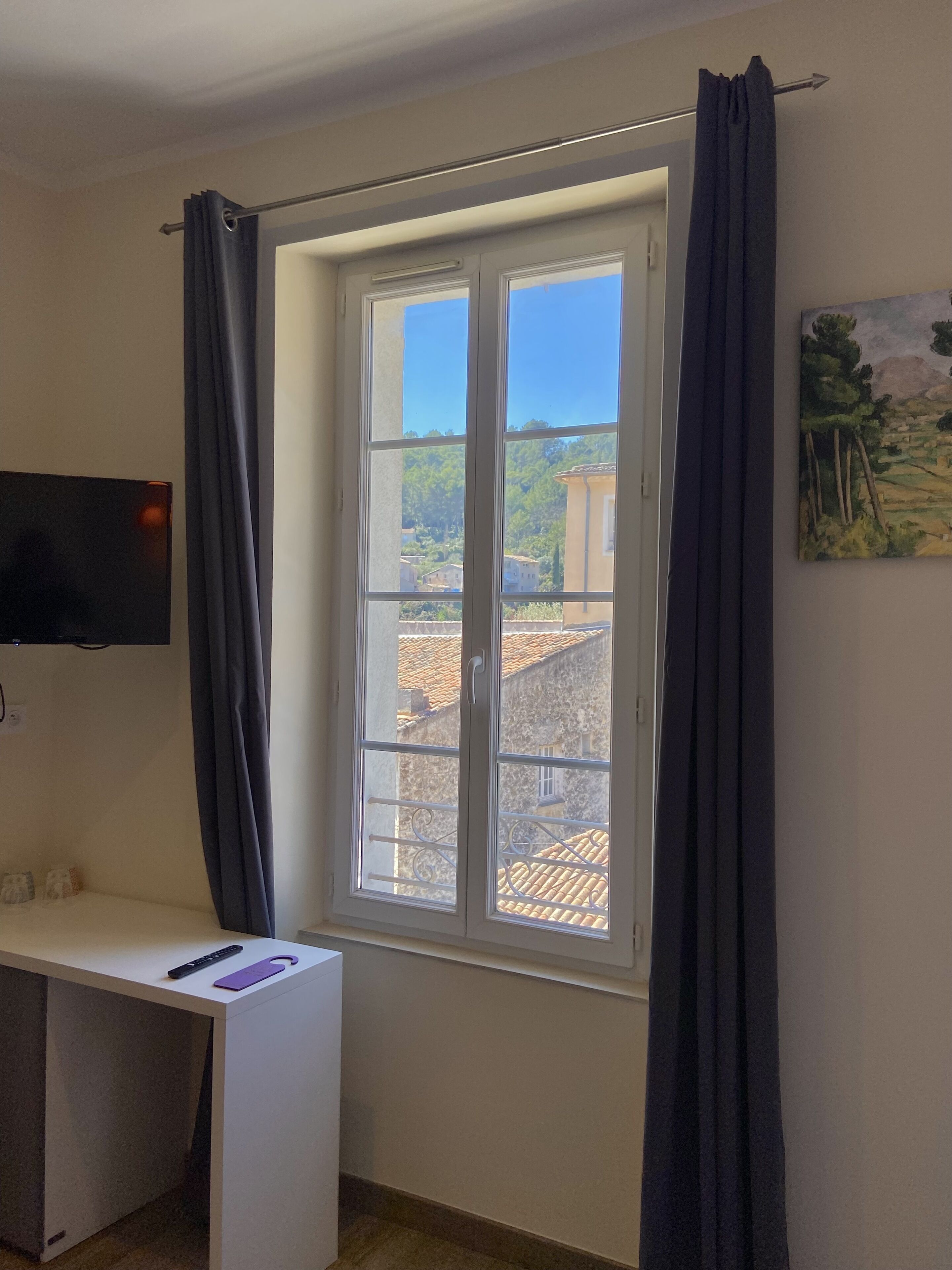 Une pièce avec une fenêtre, un bureau, une chaise et un tableau accroché au mur.