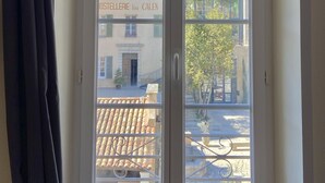 A window with a view of a building labeled "OSTELLERIE Lou CALEN" and a tree outside. - Hôtel La Falaise (Cotignac)