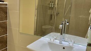 Ett badrum med en stor spegel, ett handfat och en duschhörna.