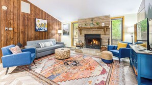 A modern living room with a stone fireplace, blue sofas, and a colorful rug.