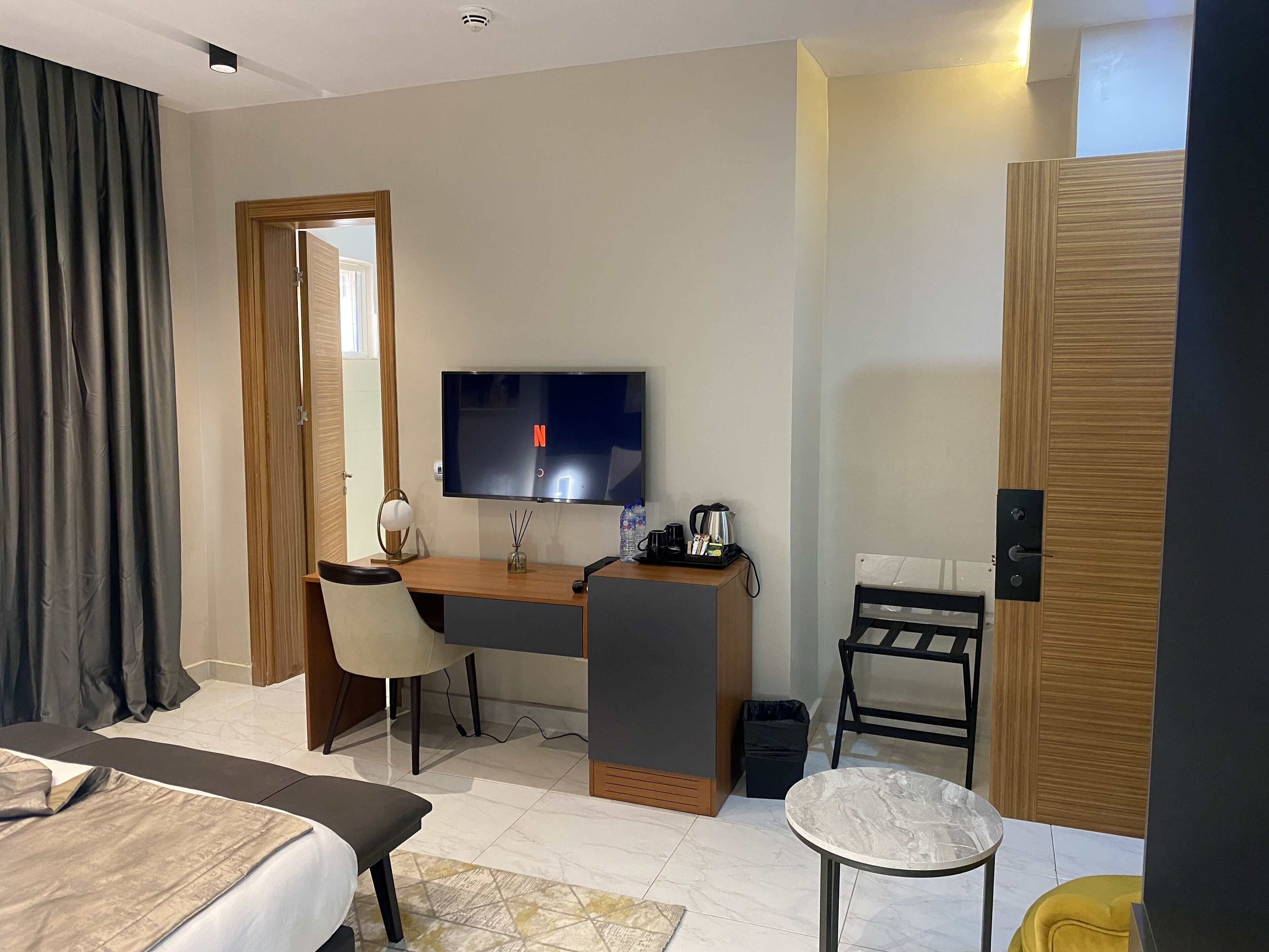 A hotel room with a bed, a desk with a chair, a television, a small table, and a door.