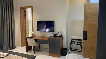 Habitación de hotel con cama, escritorio con silla, televisión, mesita y una puerta.