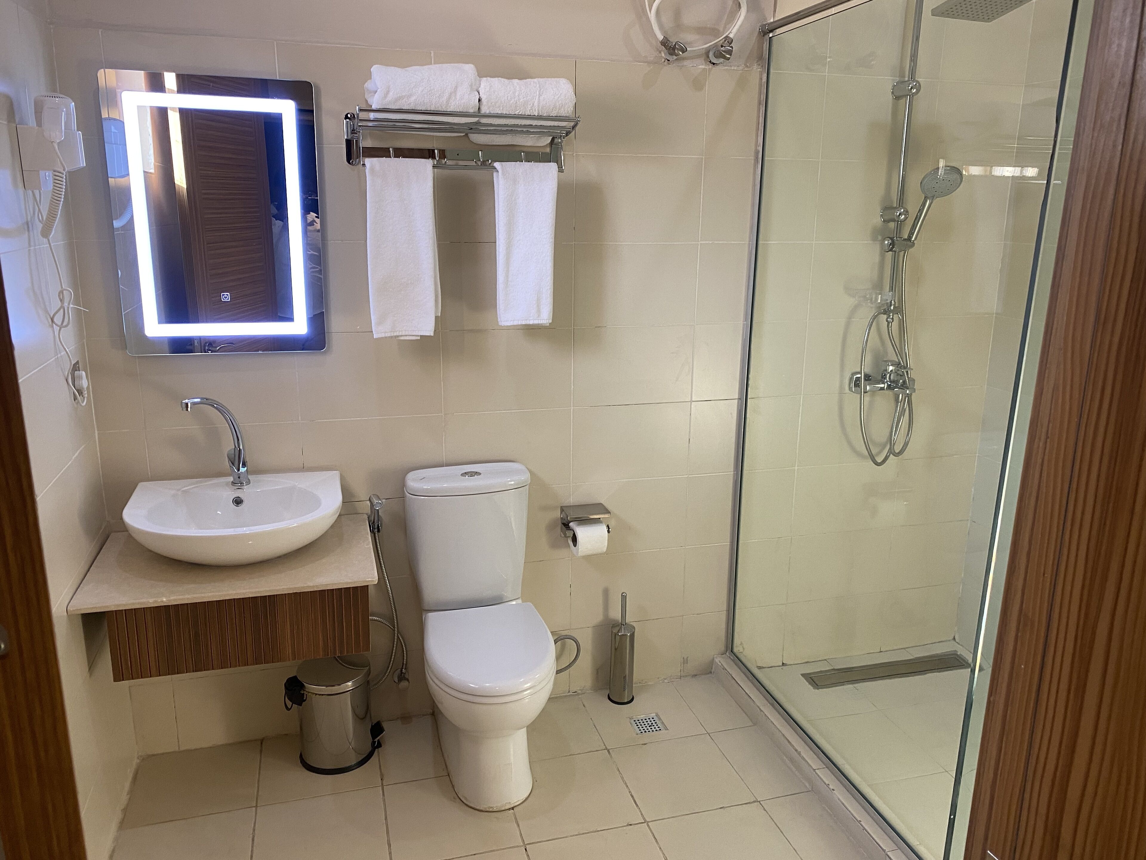 Une salle de bain moderne avec une douche à parois de verre, un lavabo, des toilettes et un miroir avec éclairage intégré.