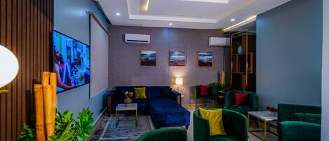 Una sala de estar moderna con un sofá azul, sillones verdes y un televisor de pantalla plana montado en la pared.