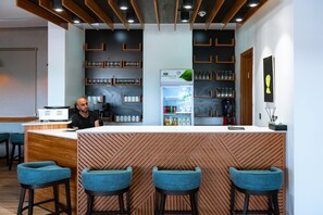 Un espace bar moderne avec un comptoir en bois, des tabourets de bar bleus et des étagères remplies de verres et de bouteilles.