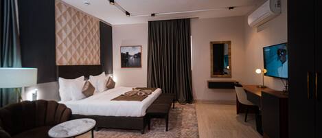 A modern hotel room with a large bed, a desk, a chair, and a TV.
