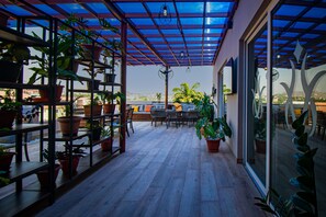 Une terrasse couverte avec un plancher en bois, des plantes en pot et du mobilier d’extérieur.