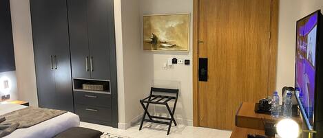 A modern hotel room with a bed, a desk with a lamp, a wooden door, and a painting on the wall.