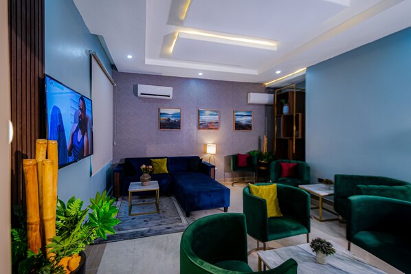 A modern living room with a sectional sofa, green armchairs, a coffee table, and a flat-screen TV.