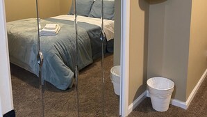 Une chambre à coucher avec un lit, un miroir, un luminaire au plafond et une poubelle.
