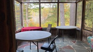Eine überdachte Terrasse mit Steinboden und zwei runden Tischen, einer mit rotem Tischlein.