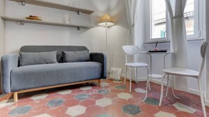 A modern living room with a grey sofa, white chairs, a floor lamp, and hexagonal patterned flooring. - APPARTAMENTO SANTI QUATTRO 1 - HOME AND MORE (Roma)