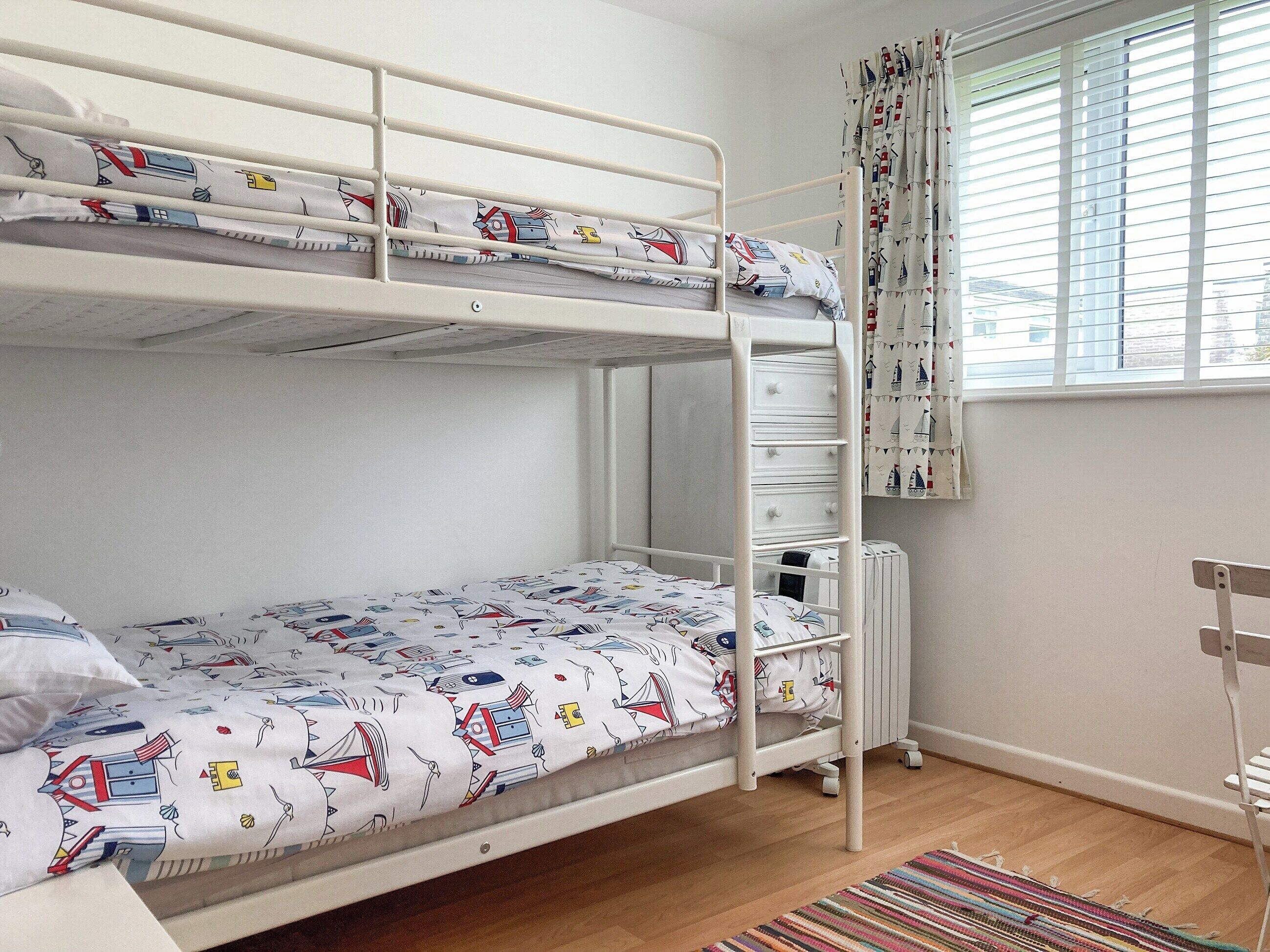 Un lit superposé avec une couvre-lit à motifs, un radiateur, une fenêtre avec des rideaux et un tapis rayé.