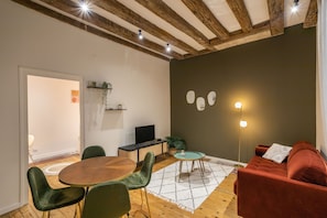 Una sala de estar moderna con techo de madera, un sofá rojo, una mesa de comedor redonda con sillas verdes y una mesita auxiliar con una planta.