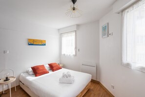 Relax in a serene bedroom with a large bed, a small table, and a window with sheer curtains.