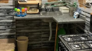 Een kleine keuken met een gasfornuis, een spoelbak en een klein aanrecht. Er staan verschillende keukenbenodigdheden en een vuilnisbak.