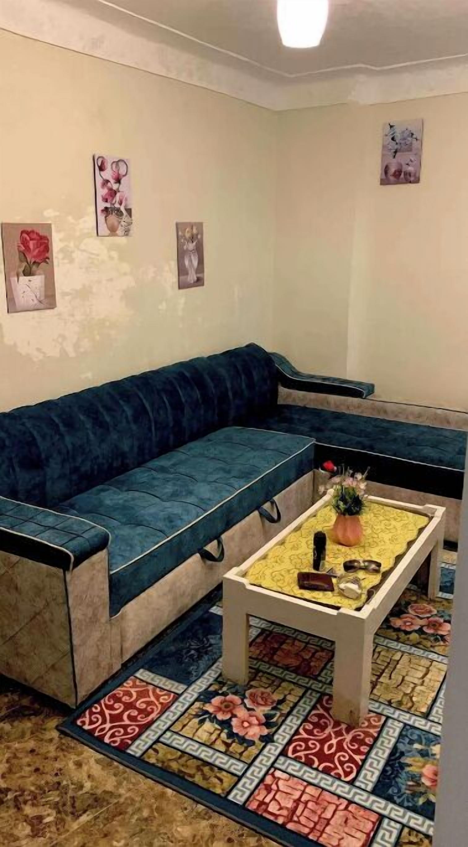 Una sala de estar con un sofá azul, una mesa de centro con camino de mesa floral y una alfombra estampada.