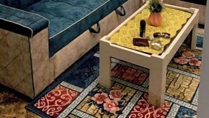 Een woonkamer met een blauwe bank, een bijzettafeltje met een bloemenloper en een kamerbreed tapijt.
