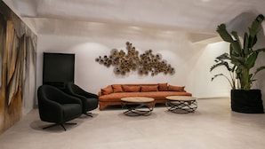 Ein modernes Wohnzimmer mit einer Couch, zwei Sesseln, einem Couchtisch und einer großen Topfpflanze.