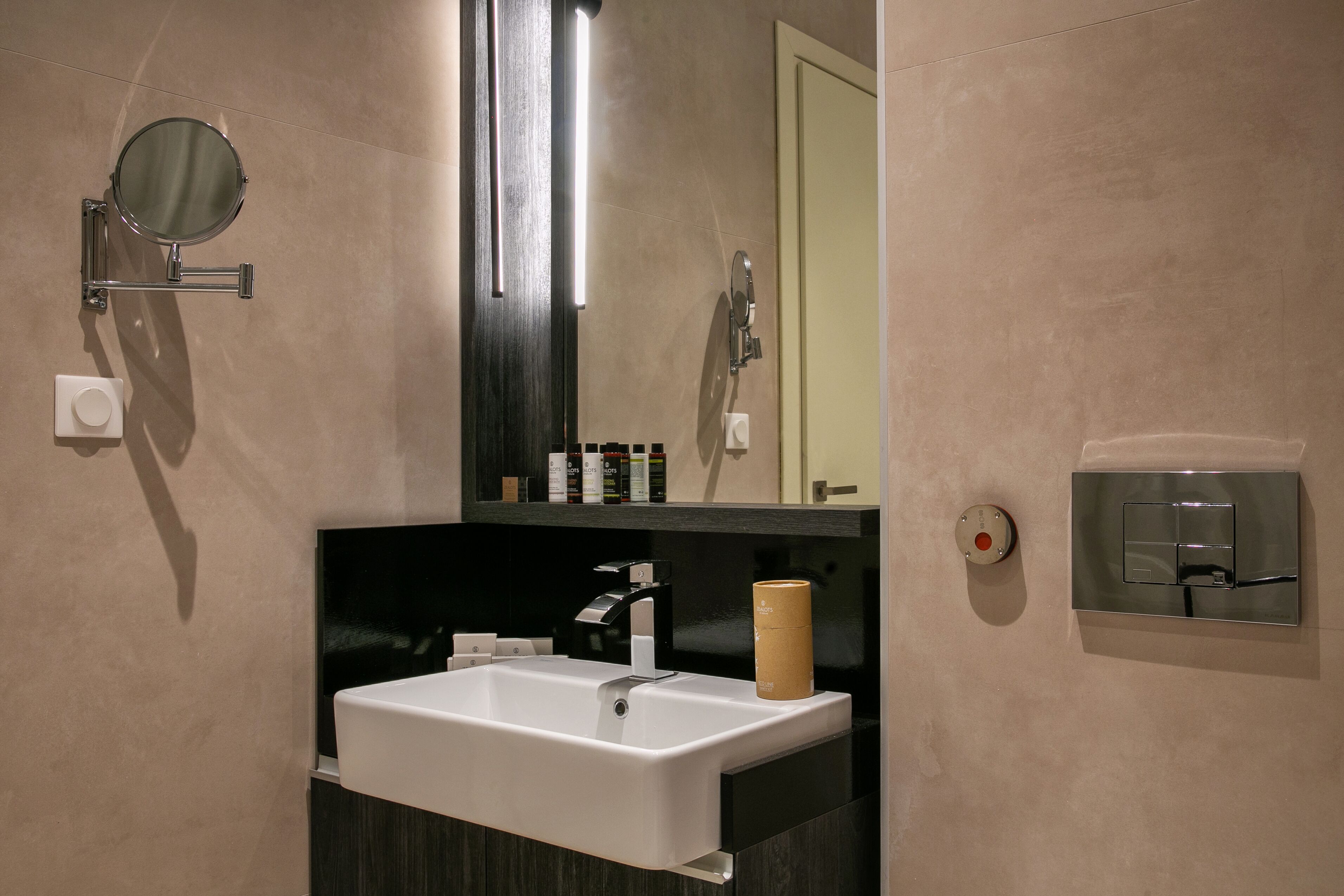 A modern bathroom with a white sink, a mirror, a towel dispenser, and a toilet paper holder.