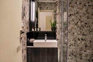 Un baño moderno con un lavabo rectangular, un espejo, una planta en maceta y una zona de ducha con puerta de cristal.