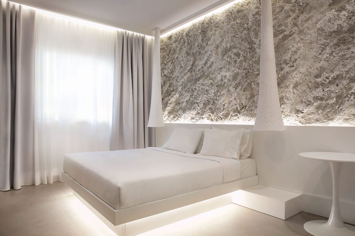Un dormitorio moderno con una cama, una mesita de noche blanca y una lámpara de pared.
