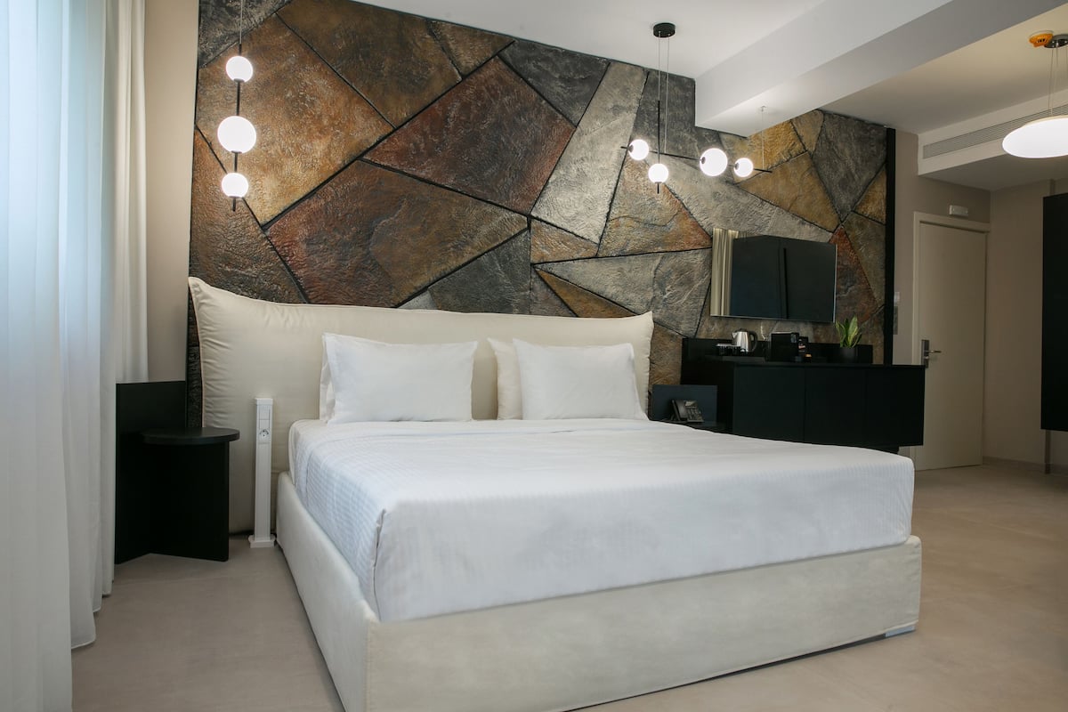 Un dormitorio moderno con una cama grande, una pared con diseño de piedra, un televisor de pantalla plana y una mesita auxiliar.