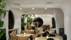 Ein modernes Restaurant mit runden Tischen und Stühlen, Zimmerpflanzen und einer zentralen Sitzgruppe.