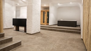 Ein geräumiger, moderner Innenraum mit minimalistischem Design, der ein großes schwarzes Klavier, eine Holzvitrine und einen Boden aus Steinplatten zeigt.