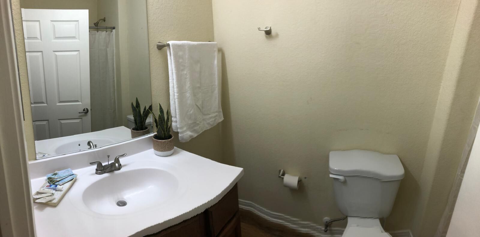 Een badkamer met een wit wastafelmeubel, spiegel, toilet en een handdoek aan de muur.