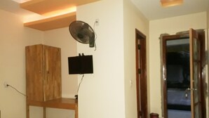 Een kamer met een bed, een houten kast, een wandtelevisie en een deur naar een andere kamer.
