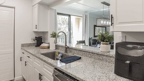 A modern kitchen with granite countertops, a stainless steel sink, and a dishwasher. There is a large window providing natural light and a view of the outdoors.