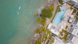 Ett flygbildsfoto av ett hotell vid stranden, med en pool, palmer och en surfbräda på sanden.
