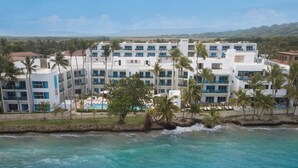 Ett semesterparadis med flera vita byggnader, palmer och ett kristallklart blått hav.