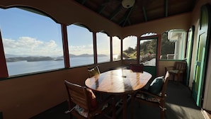 Una stanza con un tavolo grande e sedie, vista sul mare e una zona coperta con ventilatore a soffitto.