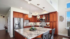 A modern kitchen with wooden cabinets, stainless steel appliances, and a marble island. - Pili Mai 7E - Top Floor 3 - Bed Suite On Golf Course - AC, Pool & Fitness Center (Koloa)