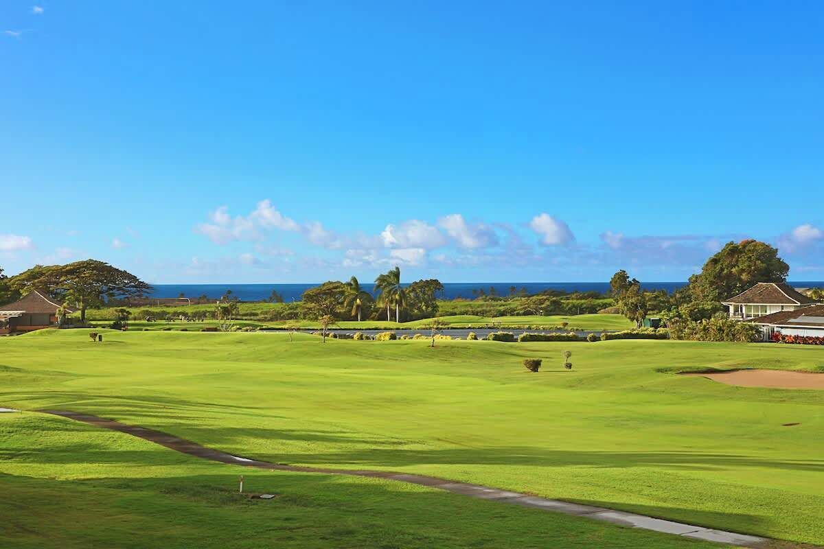 A golf course with a clear view of the ocean, a clubhouse, and a well-maintained lawn.