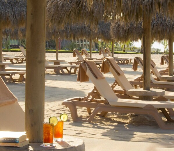 A beachside lounge area with sun loungers and thatched umbrellas.
