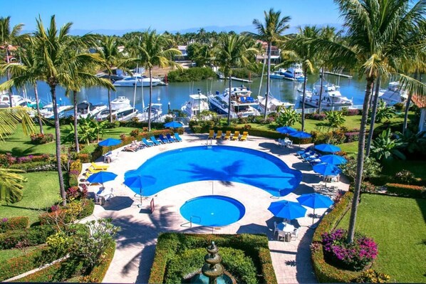 A resort with a central swimming pool, lounge chairs, and palm trees.