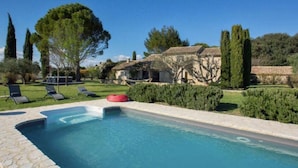 A swimming pool with lounge chairs and a red floating ring, surrounded by well-maintained hedges and tall trees.