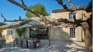 A rustic stone building with a gravel patio, outdoor seating, and a pergola.