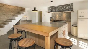 A modern kitchen with a central island, bar stools, a chalkboard with writing, a stainless steel range hood, and a white refrigerator.