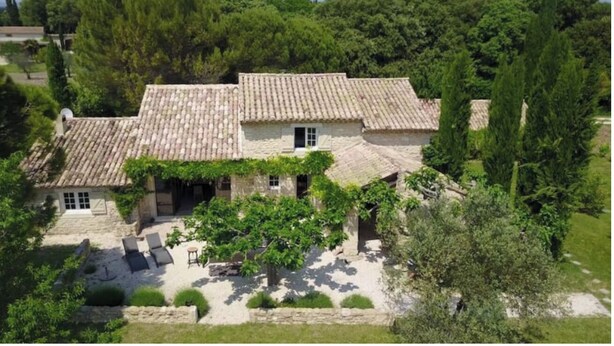 A stone building with a tiled roof, surrounded by greenery and trees.