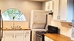 A kitchen with white cabinets, a stove, a sink, and a window with a view of greenery. - Cute 1 bedroom home, close to Downtown, Beaches and Shopping (Pensacola)