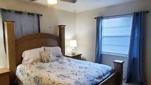 A bedroom with a bed, a nightstand, a lamp, a ceiling fan, and a window with curtains. - Cute 1 bedroom home, close to Downtown, Beaches and Shopping (Pensacola)