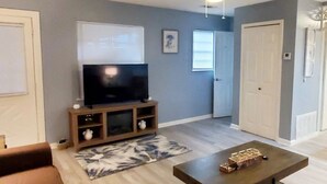 A living room with a flat-screen TV on a wooden stand, a coffee table, a patterned rug, and a ceiling fan. - Cute 1 bedroom home, close to Downtown, Beaches and Shopping (Pensacola)