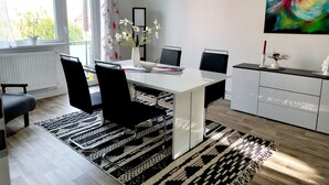 Un comedor moderno con una mesa blanca, sillas negras, un florero con flores y un cuadro en la pared.