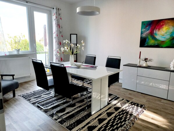 Een moderne eetruimte met een witte tafel, zwarte stoelen, een vaas met bloemen en een schilderij aan de muur.