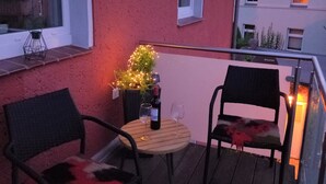 Un balcón con dos sillas, una mesita y una planta en maceta con luces.